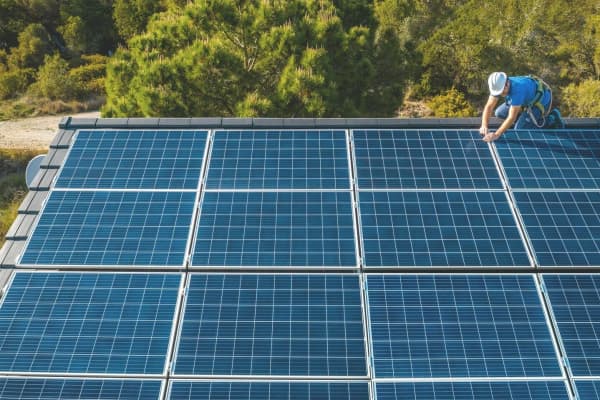 Bauarbeiter auf dem Dach, der eine große Solaranlage installiert.