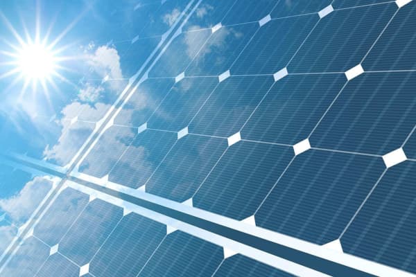 Photovoltaikmodule auf einem Schrägdach, auf die die Sonne bei blauem, leicht bewölktem Himmel scheint