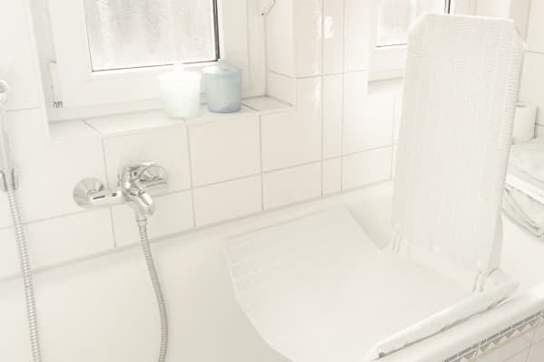 Badewanne mit Badewannenlift, Armatur und gefalteten Handtüchern in hell gefliestem Badezimmer