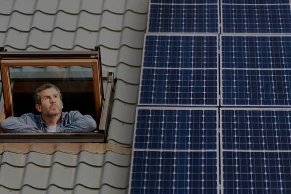 Hausdach mit großer Solaranlage, daneben ein Dachfenster aus dem eine Mann sieht