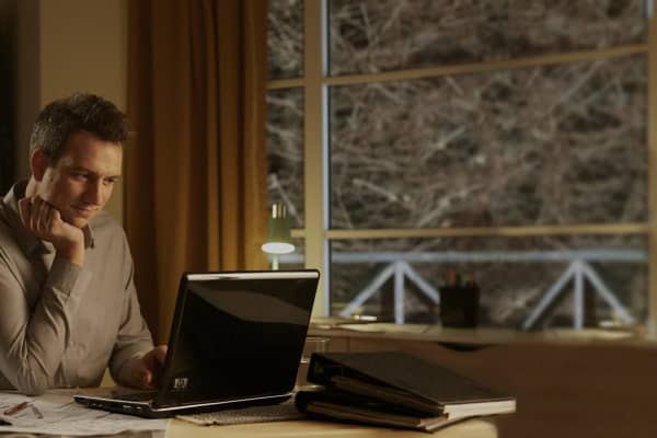 Mann sitzt am Laptop vor einem großen Fenster