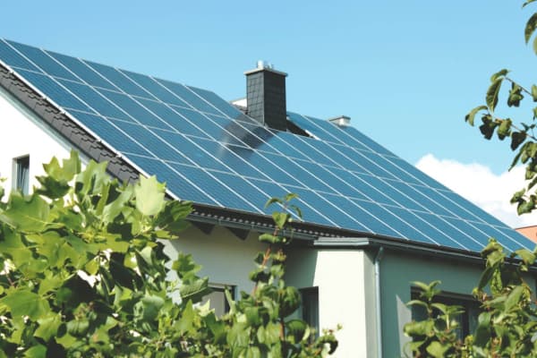 Sonnenbeschienenes Hausdach mit moderner Photovoltaikanlage in einer idyllischen Wohngegend. Nachhaltige Energiegewinnung inmitten von grüner Natur.
