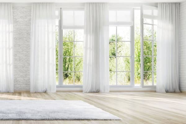 Helle Wohnraumansicht mit großen Sprossenfenstern, weißen Vorhängen und Parkettboden