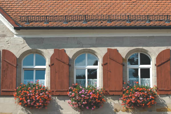 Rundbogenfenster an historischer Steinfassade mit Holzläden und roten Dachziegeln