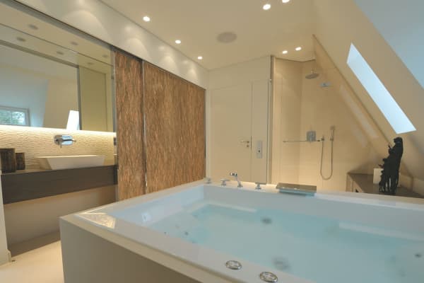 Eine eckige, große Whirlpool Badewanne für 2 Personen in einem modernen schlichtem Badezimmer mit warmem Licht