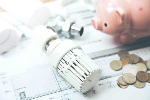 Thermostat einer Heizung liegt neben Kleingeld und Sparschwein auf Plänen.