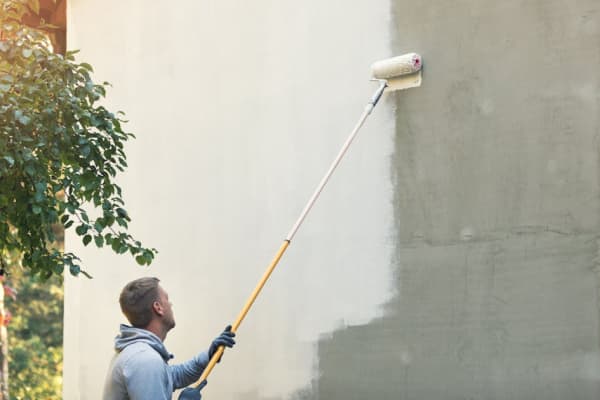 Mann streicht eine Hausfassade weiß an