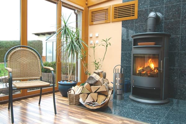 Wintergarten mit Holzofen und großen Fensterfronten.