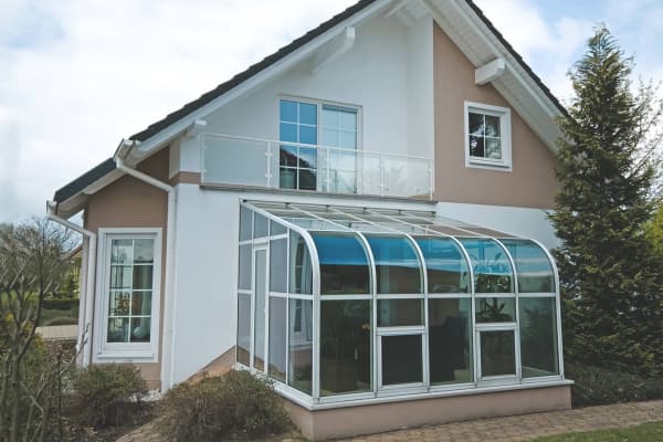 Wintergarten mit Rundbogendach, der an ein Einfamilienhaus angebaut ist.