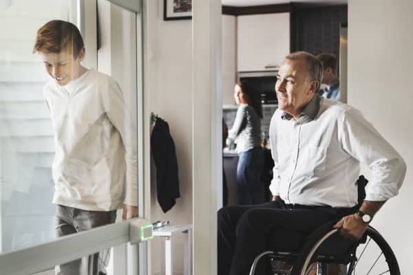 Ein älterer Mann im Rollstuhl zu Hause mit seinen Kindern und Enkel vor Rollstuhllift.