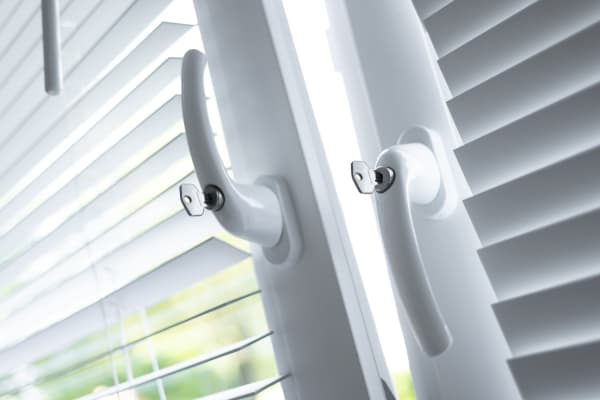Zwei Fenster mit weißen Rollos und Sicherheitsgriffen, davon ist das linke gekippt