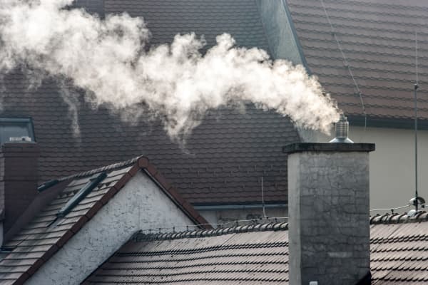 Schornstein mit Rauch vor grauen Wohnhäusern
