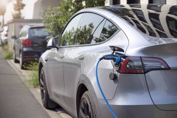 Silbernes Elektroauto am Straßenrand mit eingestecktem Ladestecker
