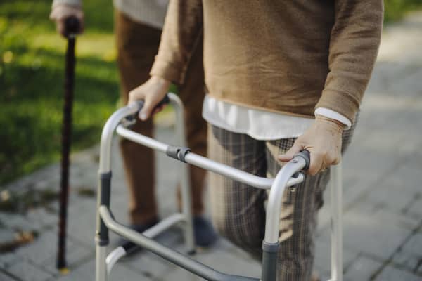 Senior und Seniorin mit Gehhilfe auf gepflastertem Weg