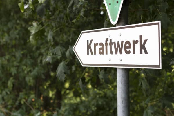 Richtungsweisendes Schild mit der Aufschrift Kraftwerk vor grünen Büschen