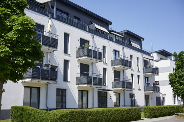 Modernes Mehrfamilienhaus mit weißer Fassade und Balkonen, davor eine gepflegte, grüne Hecke