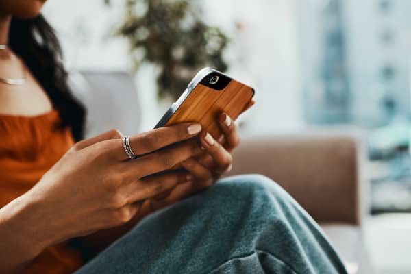 Junge Frau mit Smartphone in der Hand sitzt in Wohnung