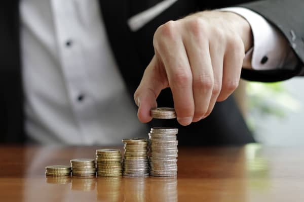 Mann in Hemd und Sakko stapelt Münzen auf ansteigend hohe Stapel auf einem Tisch