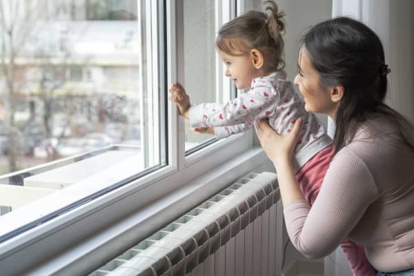 Mutter und Kleinkind schauen aus einem Fenster in einer Wohnung