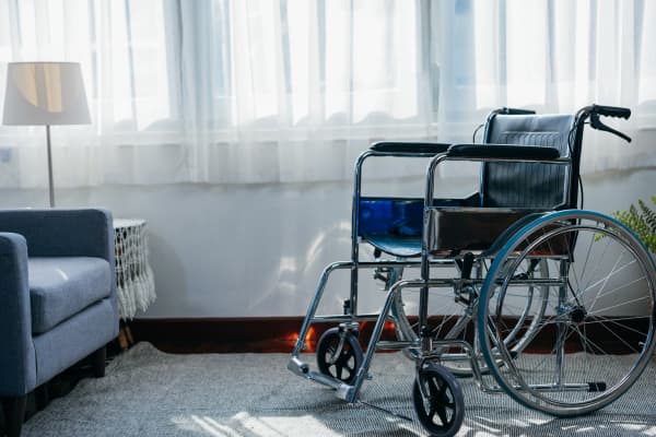 Rollstuhl auf einem Teppich neben einem blauen Sessel vor einem Fenster