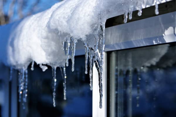 Schnee und Eiszapfen auf dem Dach über einem Fenster