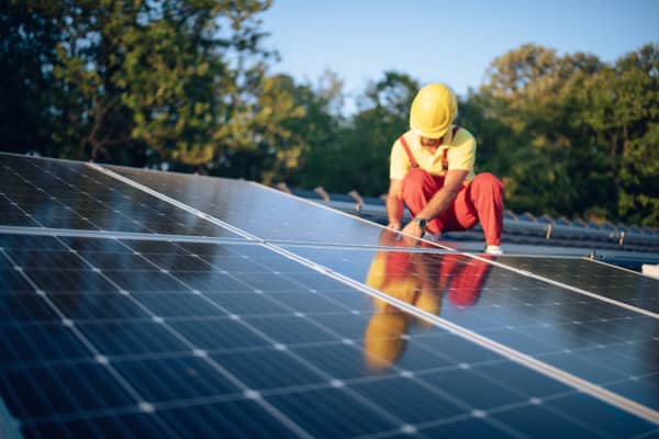 Monteur mit roter Arbeitshose und gelbem Helm montiert eine Solaranlage auf dem Dach