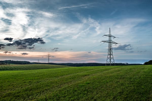 Strommasten auf grüner Wiese vor bewölktem Himmel