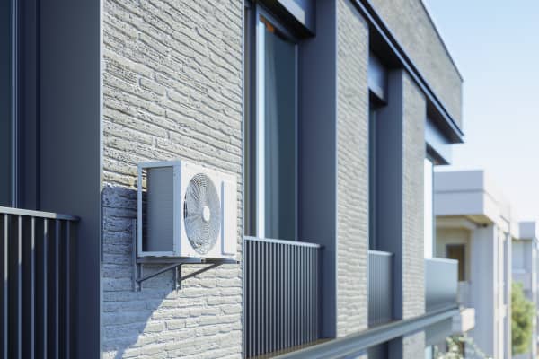 Wärmepumpe an der Fassade eines Mehrfamilienhauses zwischen zwei Balkonen