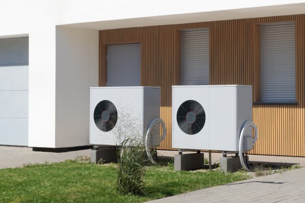 Zwei Luftwärmepumpen auf kleiner Rasenfläche vor Haus mit Holzvertäfelung an der Fassade