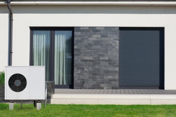 Luft-Wärmepumpe auf grüner Wiese vor der Terrasse eines modernen Wohnhauses