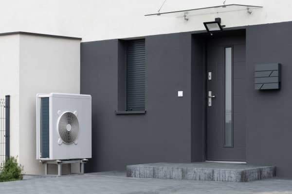 Weiße Luft-Wärmepumpe auf Sockel steht an modernem, dunklem Wohnhaus