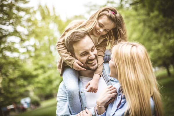 Junges lachendes Paar im Grünen, der Vater hat seine Tochter auf den Schultern
