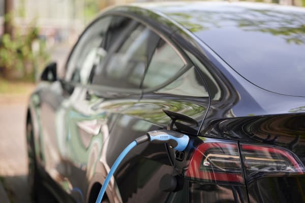 Ansicht eines schwarzen Elektroautos von hinten links mit angeschlossenem Ladekabel