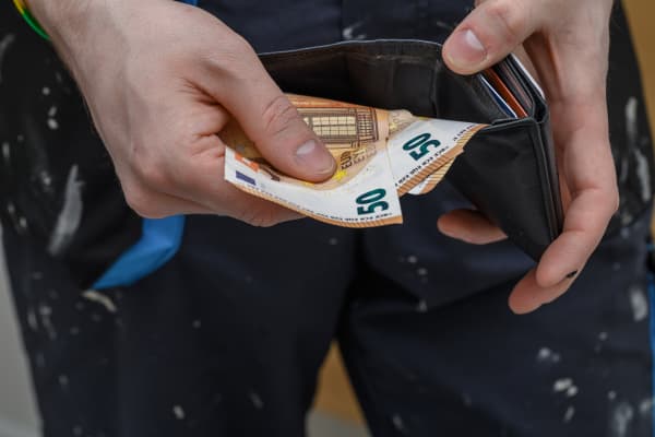 Ein Handwerker hält Geld und ein Portemonnaie in den Händen.