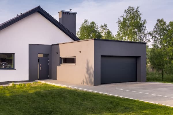 Garage aus Beton mit Seitenfenster und Sektionaltor vor einem Einfamilienhaus.