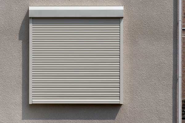 Ein geschlossener Rollladen aus Kunststoff von außen an einem Fenster.