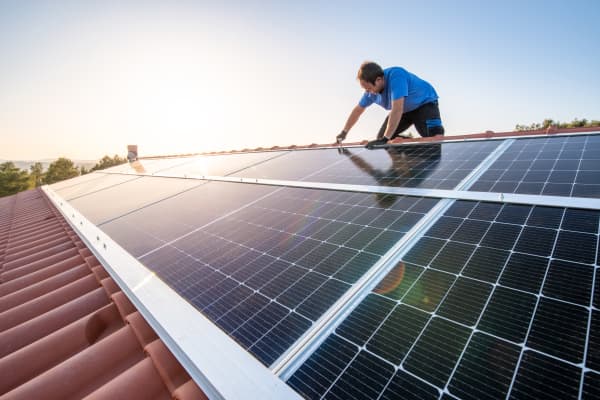 Handwerker installiert Solarmodule auf einem Schrägdach mit Ziegeln bei strahlendem Sonnenschein