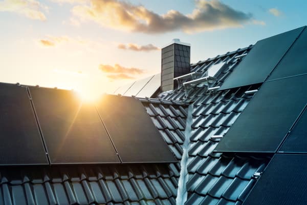 Schwarz gedecktes Wohnhausdach mit schwarzen Solarmodulen, hinter denen die Sonne zu sehen ist