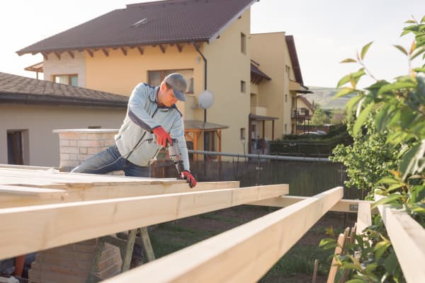 Ein Mann ist dabei, die Holzbalken einer Terrassenüberdachung selbst zu bauen.