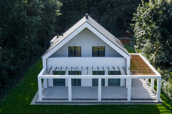 Modernes Haus mit einer L-förmigen Pergola umgeben von hohen Bäumen