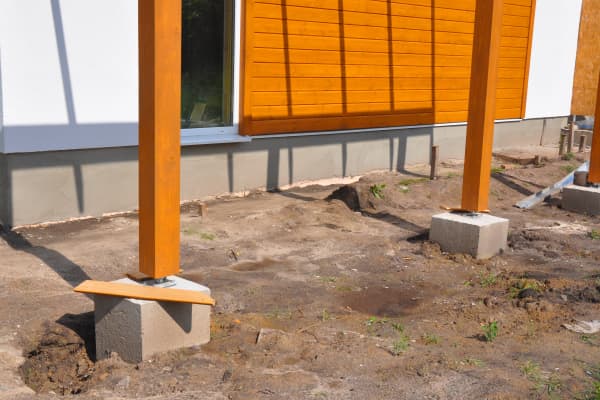 Holzpfosten vor einer Hauswand sind auf dem Fundament der Terrassenüberdachung verschraubt.
