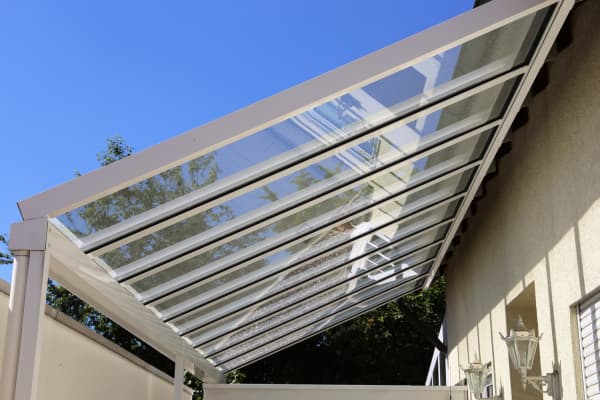 Terrassenüberdachung aus Glas und Aluminium mit Neigung an eine Hauswand gebaut.