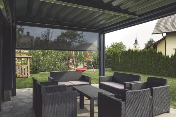Terrassenüberdachung mit Sitzgruppe und einem halb heruntergefahrenen Seitenrollo