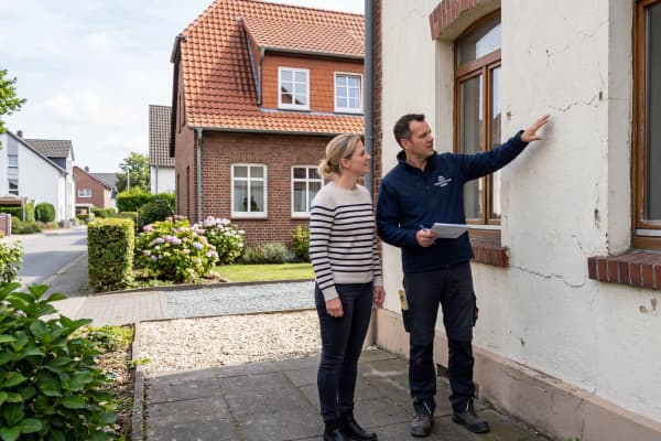 Ein Fachberater begutachtet gemeinsam mit einer Hausbesitzerin den Zustand einer Hausfassade. Das Bild zeigt eine realistische Vor-Ort-Beratung zur Planung einer Fassadendämmung.