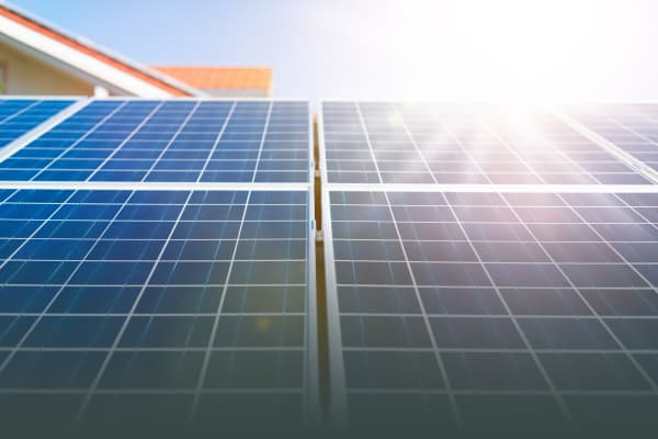 Nahaufnahme von blauen Solarmodulen mit einem klaren Rastermuster, beleuchtet von hellem Sonnenlicht. Die Module gehören zu einer Solaranlage auf einem Wohnhaus und erzeugen erneuerbare Energie zur nachhaltigen Stromversorgung.