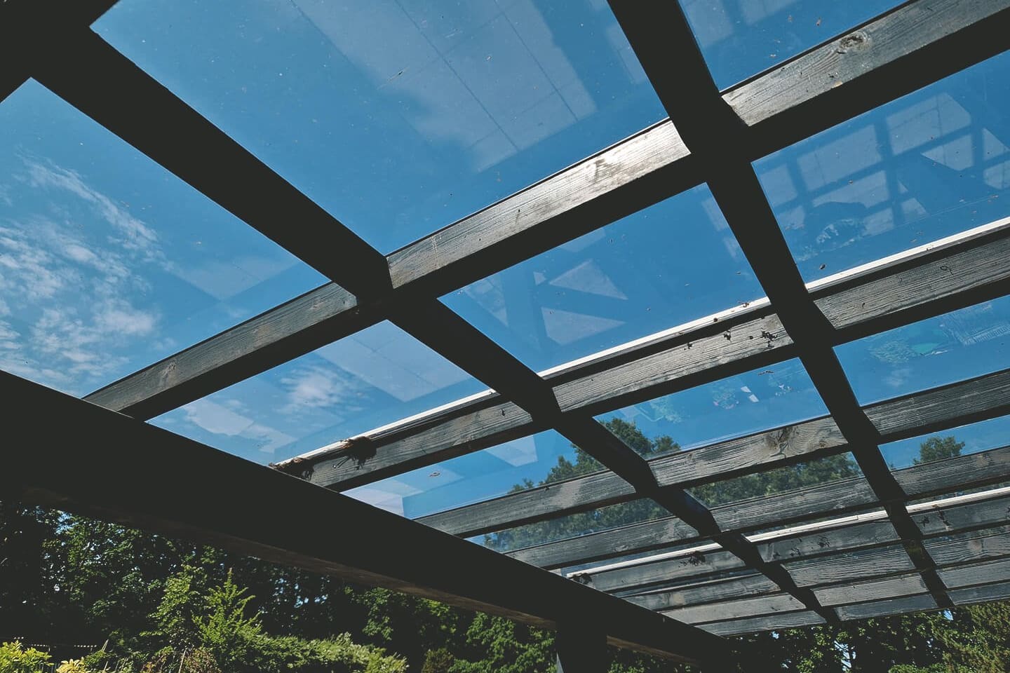 Terrassenüberdachung mit Glasdach und Holzrahmen bei blauem Himmel.