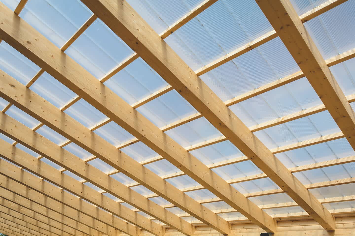 Terrassenüberdachung aus Holzkonstruktion mit transparenten Paneelen.
