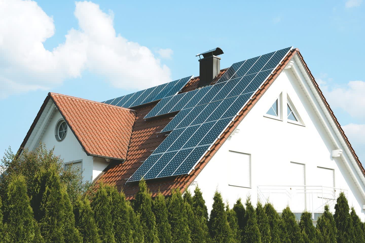 Haus mit Photovoltaik in Brandenburg vor blauem Himmel mit weißen Wolken und hinter einer grünen Hecke