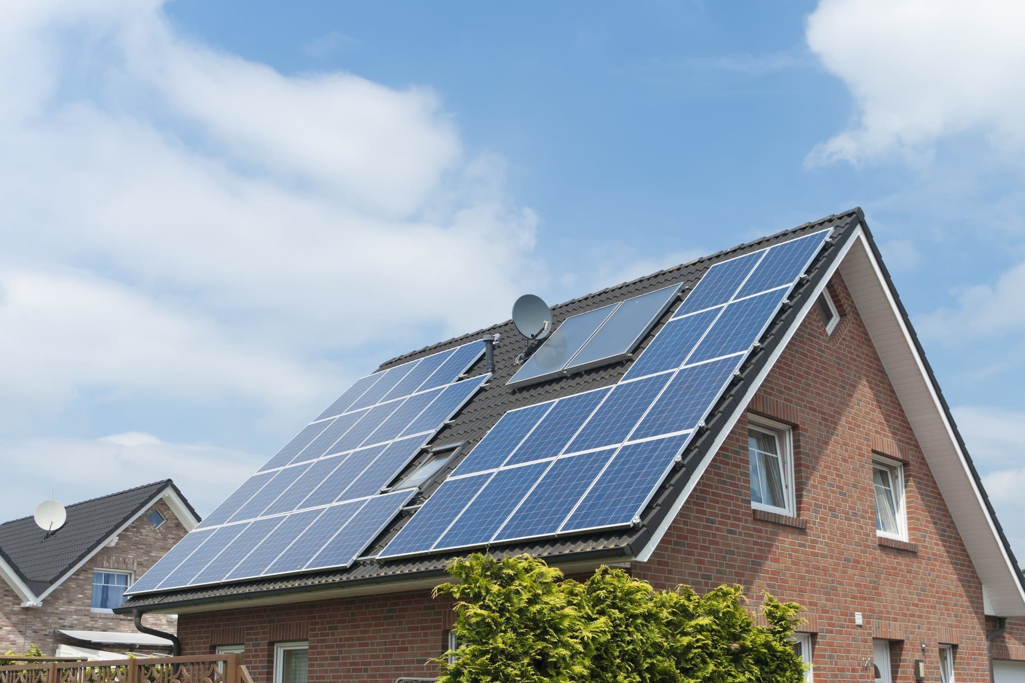 Einfamilienhaus aus rotem Backstein mit großer Photovoltaikanlage auf dem Dach vor blauem Himmel und weißen Wolken
