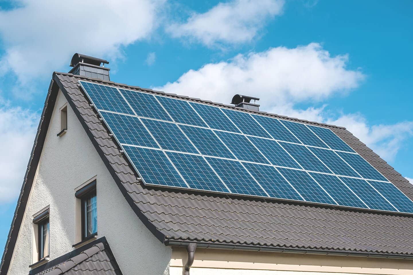 Einfamilienhaus mit Solaranlage auf grauem Dach vor blauem Himmel mit weißen Wolken